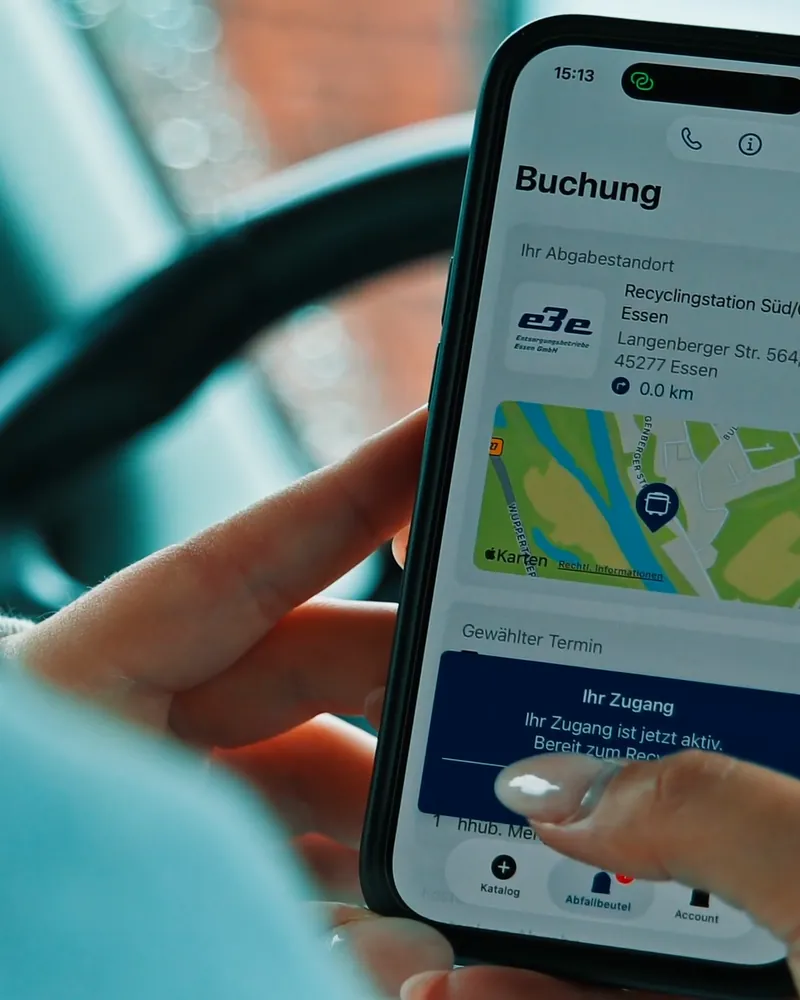 Hand mit Smartphone im Auto, in der MAEX-App ist die gebuchte Zeit an der Recyclingstation geöffnet