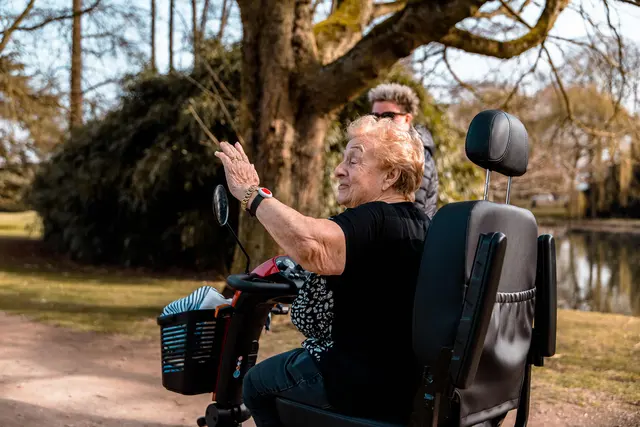 Seniorin im Elektromobil zeigt am See auf etwas in den Bäumen