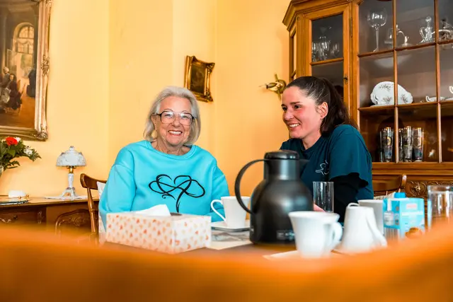 Seniorin und Betreuungskraft beim Kaffee am gedeckten Tisch