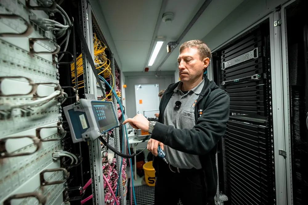 Techniker misst an einem Netzwerkschrank mit Glasfaserkabeln