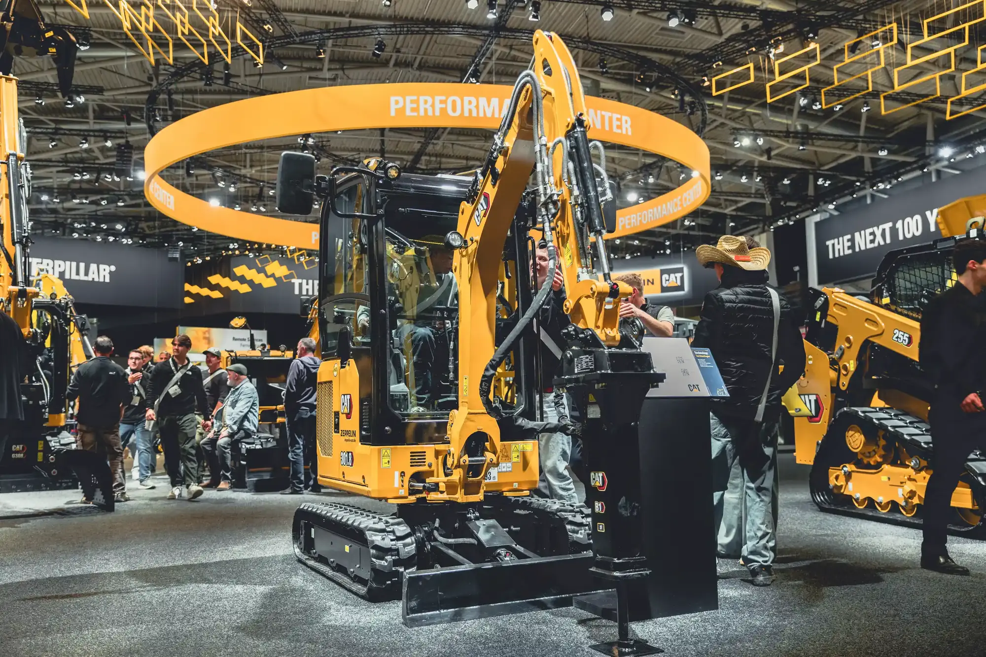 Besucher in der Caterpillar-Halle der bauma 2025 rund um einen Bagger unter dem Ring des Performance Centers