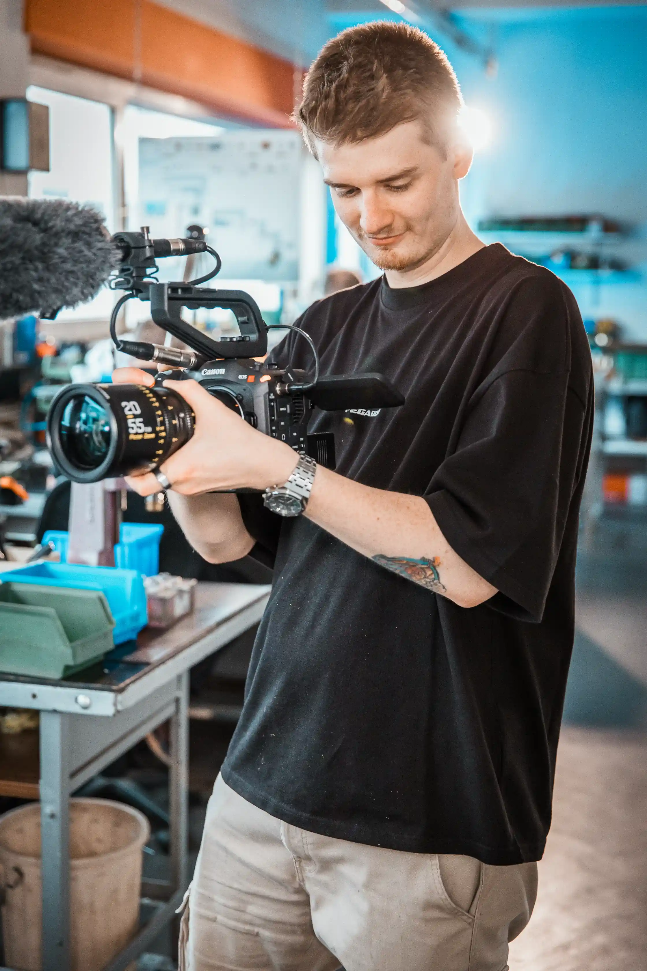 Behind the Scenes · Junger CreativCube-Filmemacher mit Kamera in Werkstatt-Setting